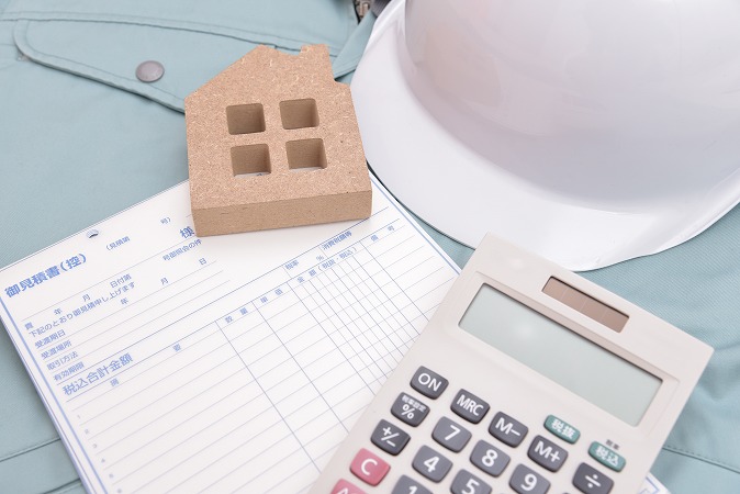作業着の上に見積書と電卓と家の模型
